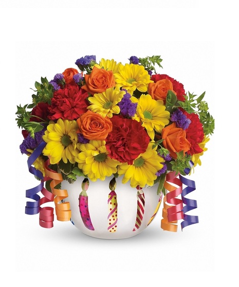 Birthday gift of bright flowers in a frosted glass bowl adorned with a shiny birthday candle motif, and ribbons. 
